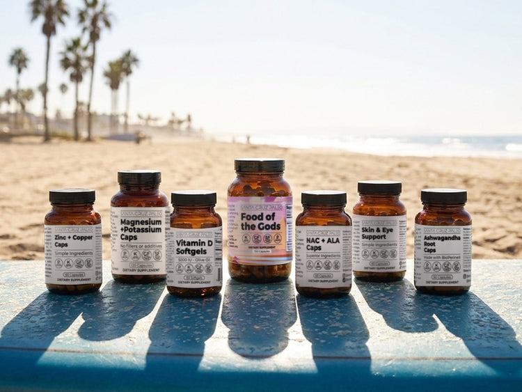 Seven Santa Cruz Paleo supplement bottles lined up on a surfboard at the beach