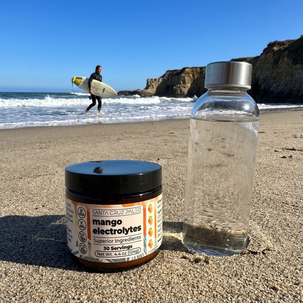 Electrolytes tub and water bottle on the beach, a surfer behind