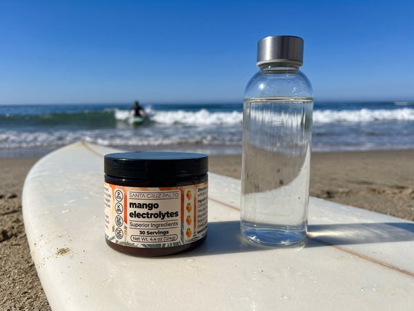 The Mango tub and a glass water bottle on a surfboard at the beach