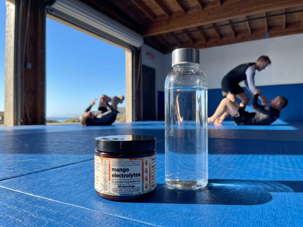 The Mango tub and a glass water bottle on a training mat, two people grappling behind
